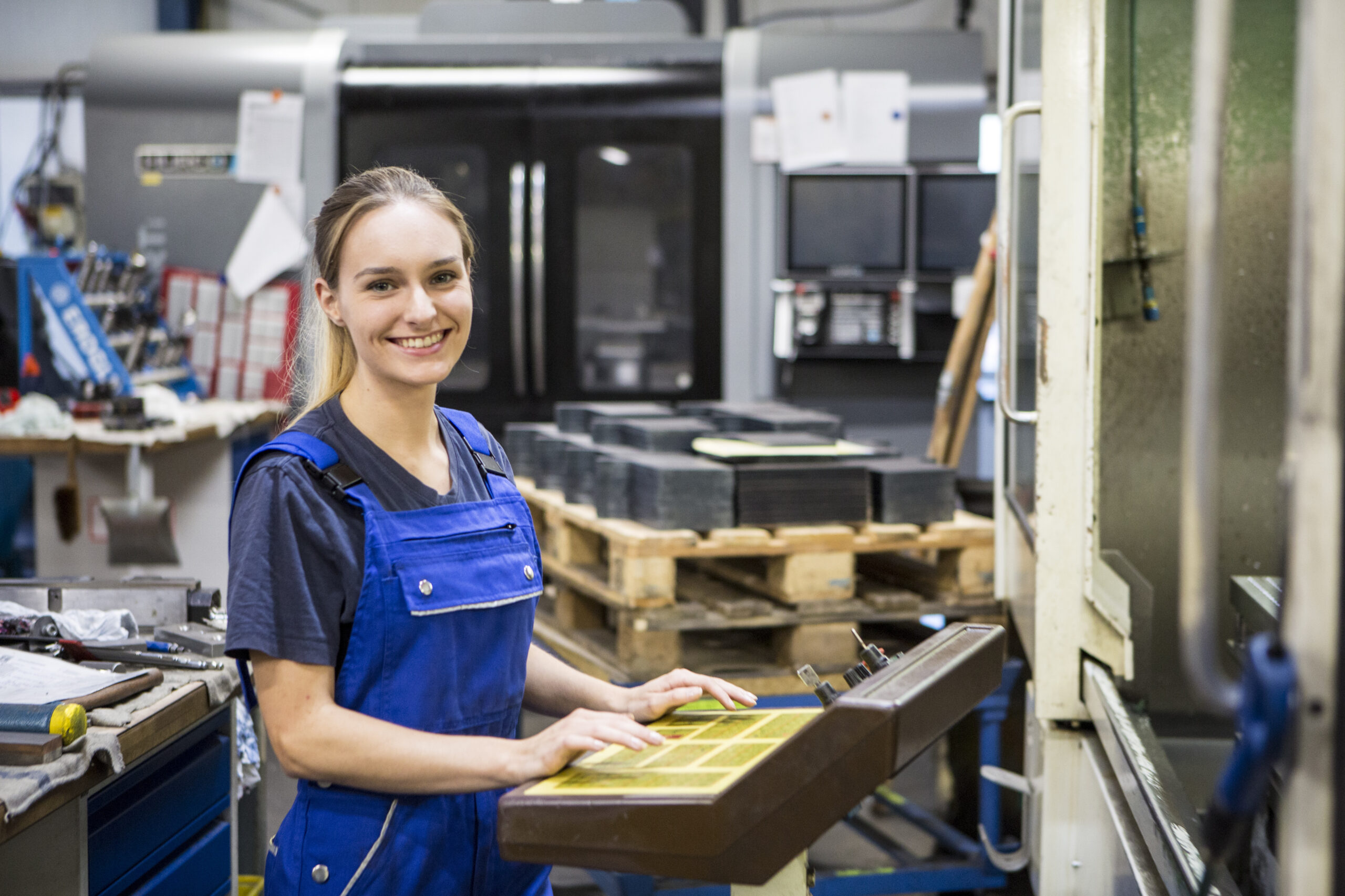 Eine junge Handwerkerin in blauer Latzhose bedient eine Maschine