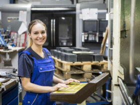 Eine junge Frau in blauer Latzhose bedient eine Maschine in einem Handwerksbetrieb